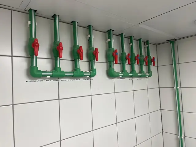 Colectores de agua caliente sanitaria y agua fría con llaves rotuladas por zona en un cuarto técnico alicatado
