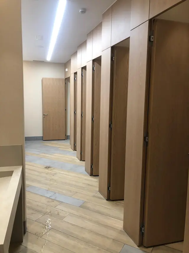 Pasillo de cabinas con puertas de madera hasta el techo en unos aseos de local