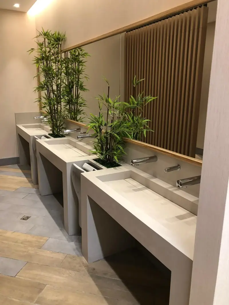 Lavabos corridos con grifería electrónica, secamanos integrados y jardineras en unos aseos públicos