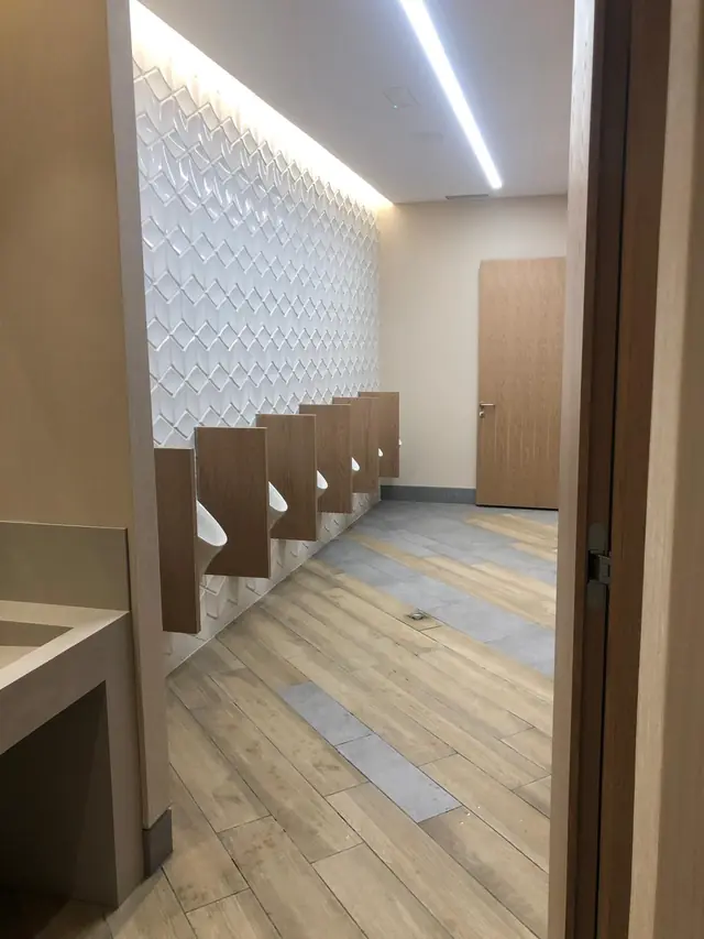Urinarios con separadores de madera sobre pared de azulejo 3D e iluminación indirecta
