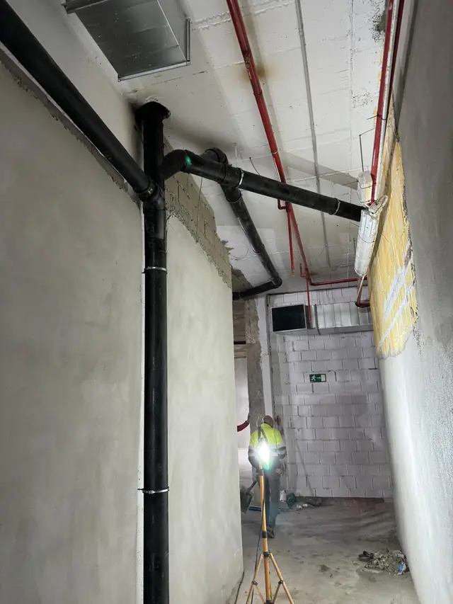 Bajante de polietileno y colector colgado del techo en el pasillo técnico de un local en obra