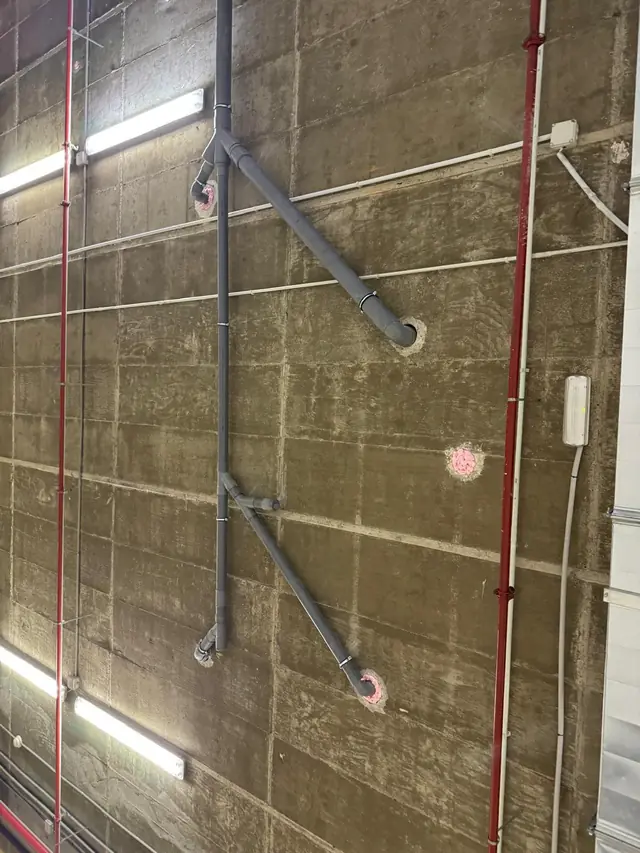 Bajante y ramales de PVC anclados a un muro de hormigón en un aparcamiento
